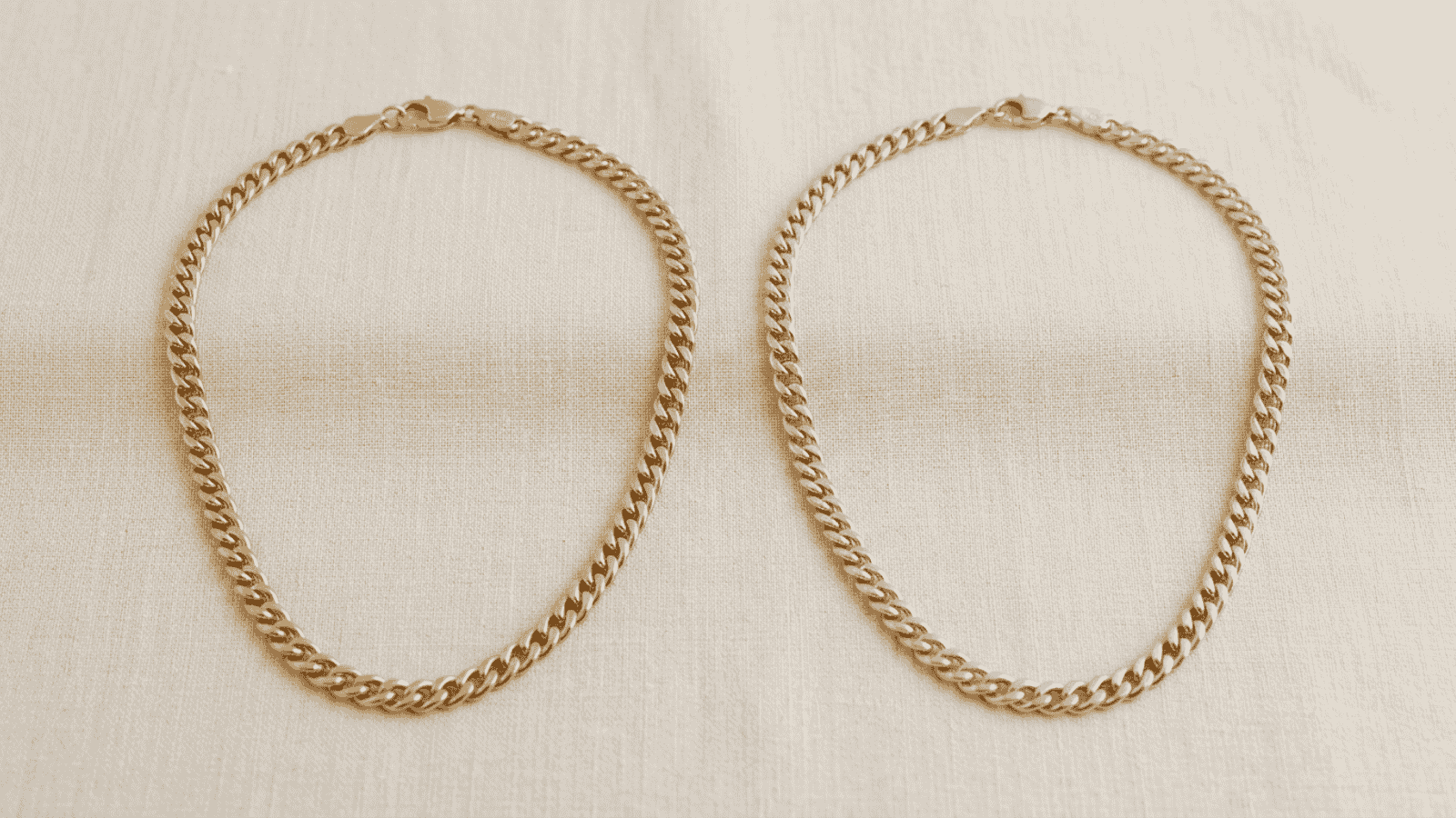 Side by side comparison of 18K and 14K gold plated chain necklaces on soft cream background showing the color difference
