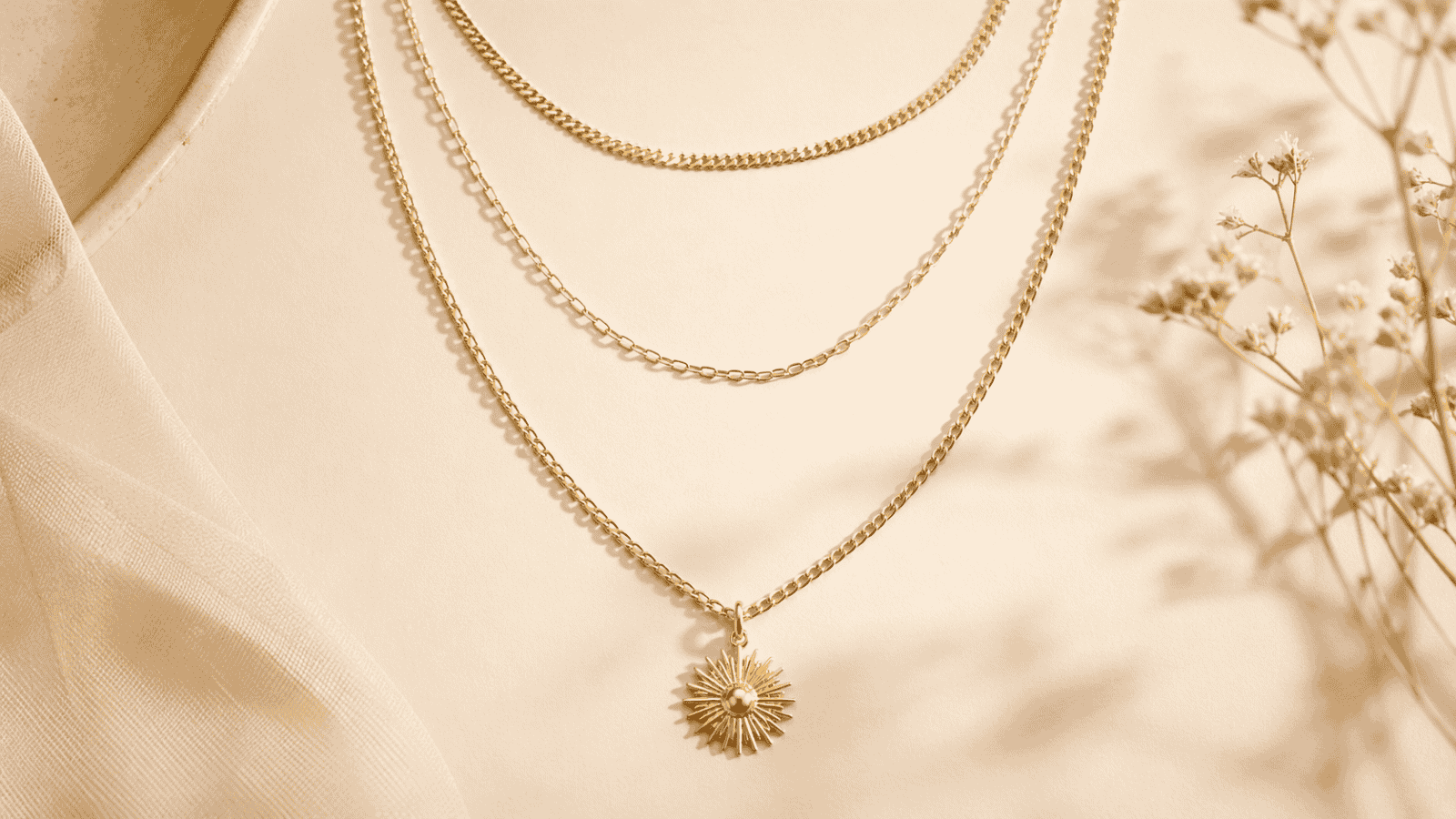 Layered gold plated necklaces at three lengths including choker, princess, and matinee chains with a pendant focal point on cream background