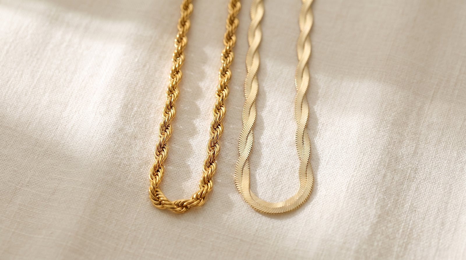 Two dainty gold-plated chain necklaces side by side on cream linen, warmer 18K next to a paler 14K tone