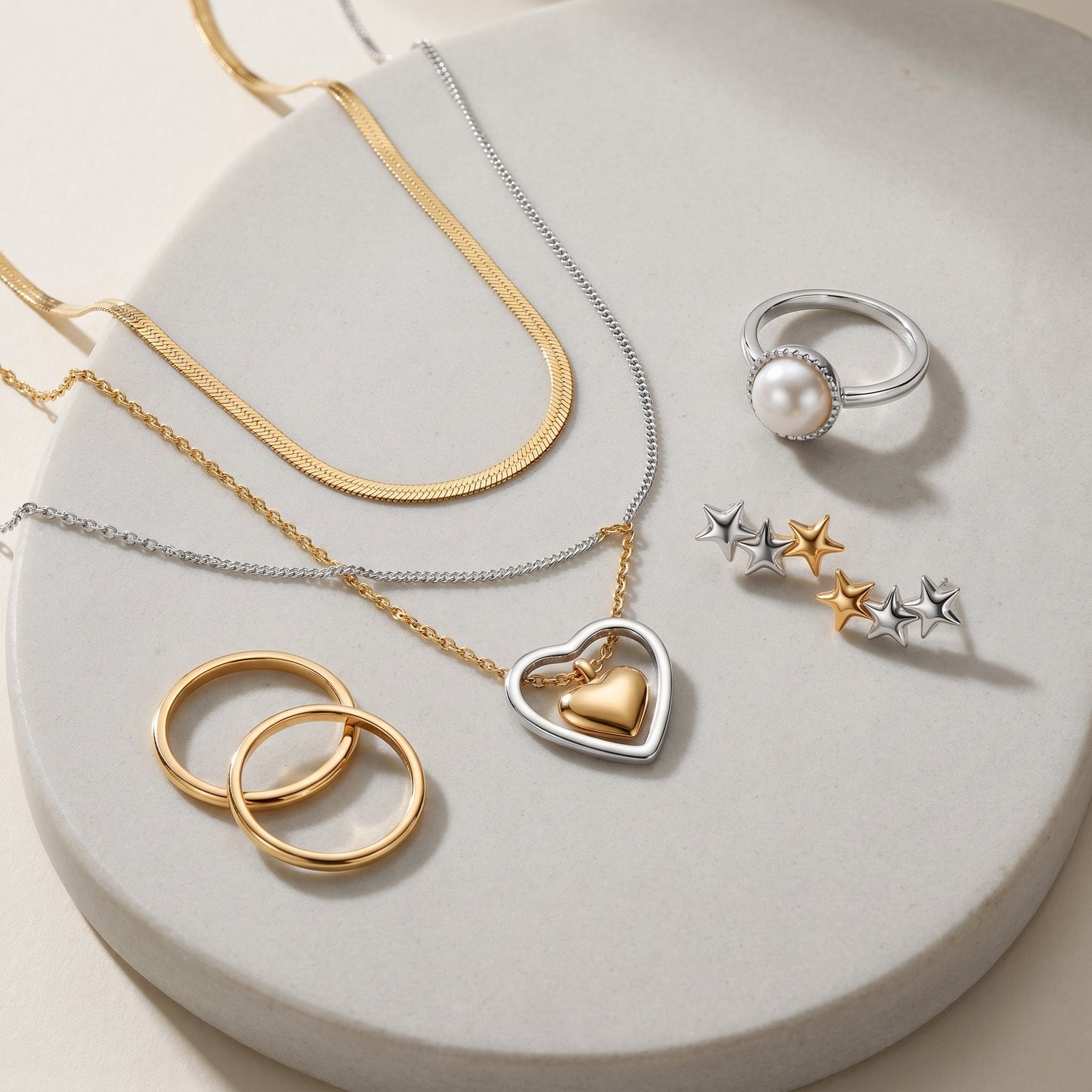 Flat-lay on grey stone of yellow gold plated necklaces and rings with a single silver accent chain