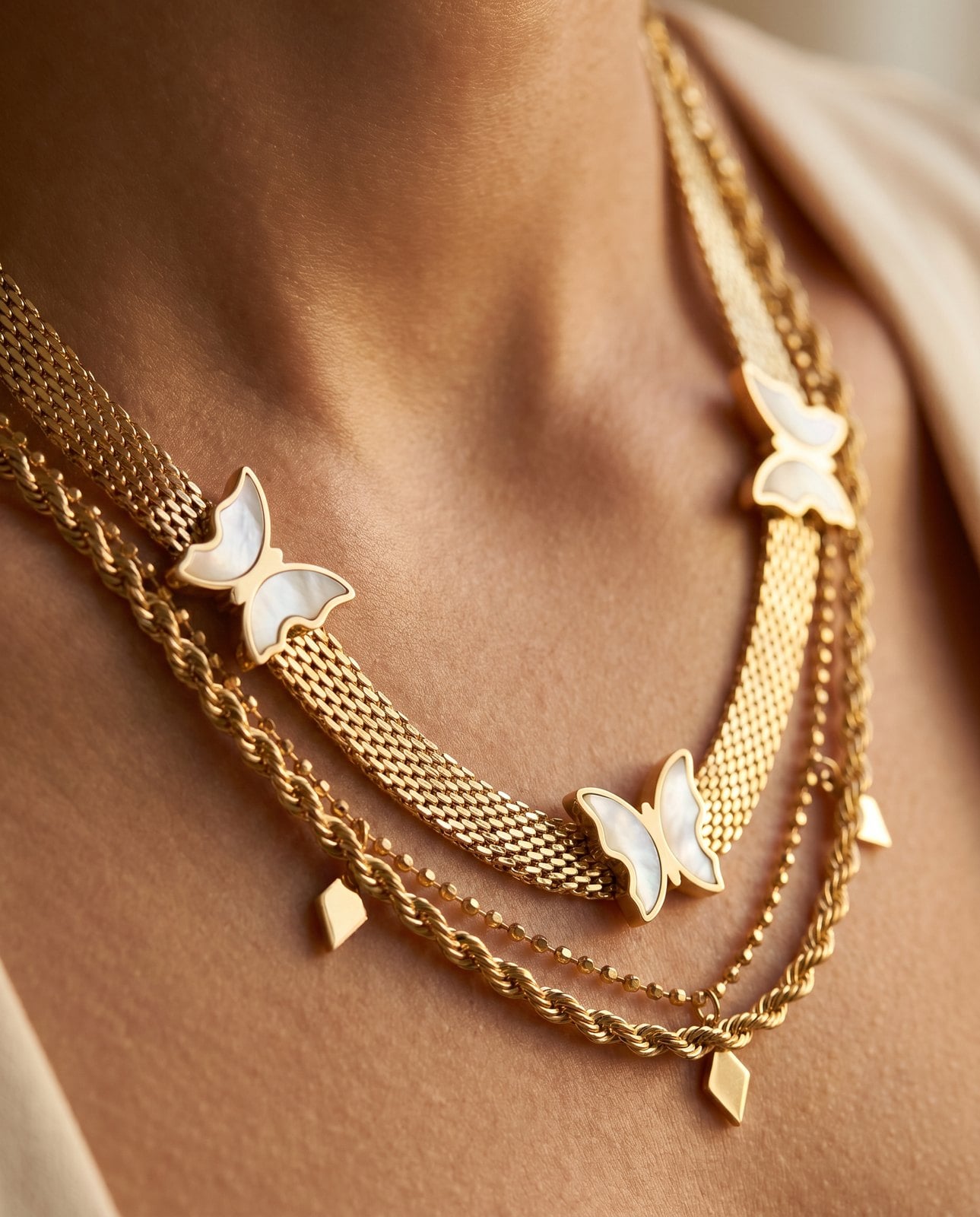Extreme close-up of a thick herringbone gold plated chain layered with a finer pendant chain on warm skin