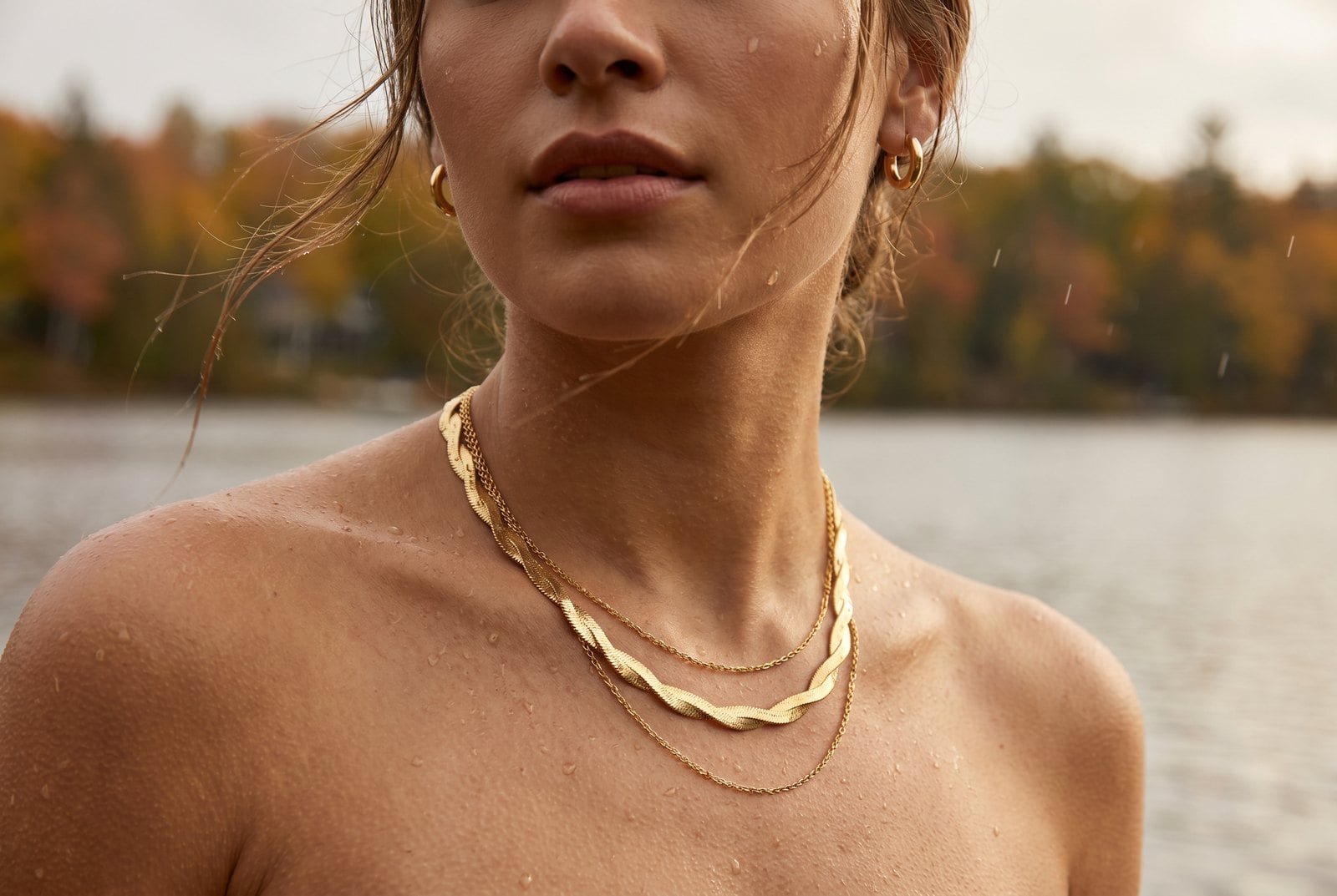 Model by a lake in autumn wearing gold plated chains with water droplets on her skin, showing everyday wear
