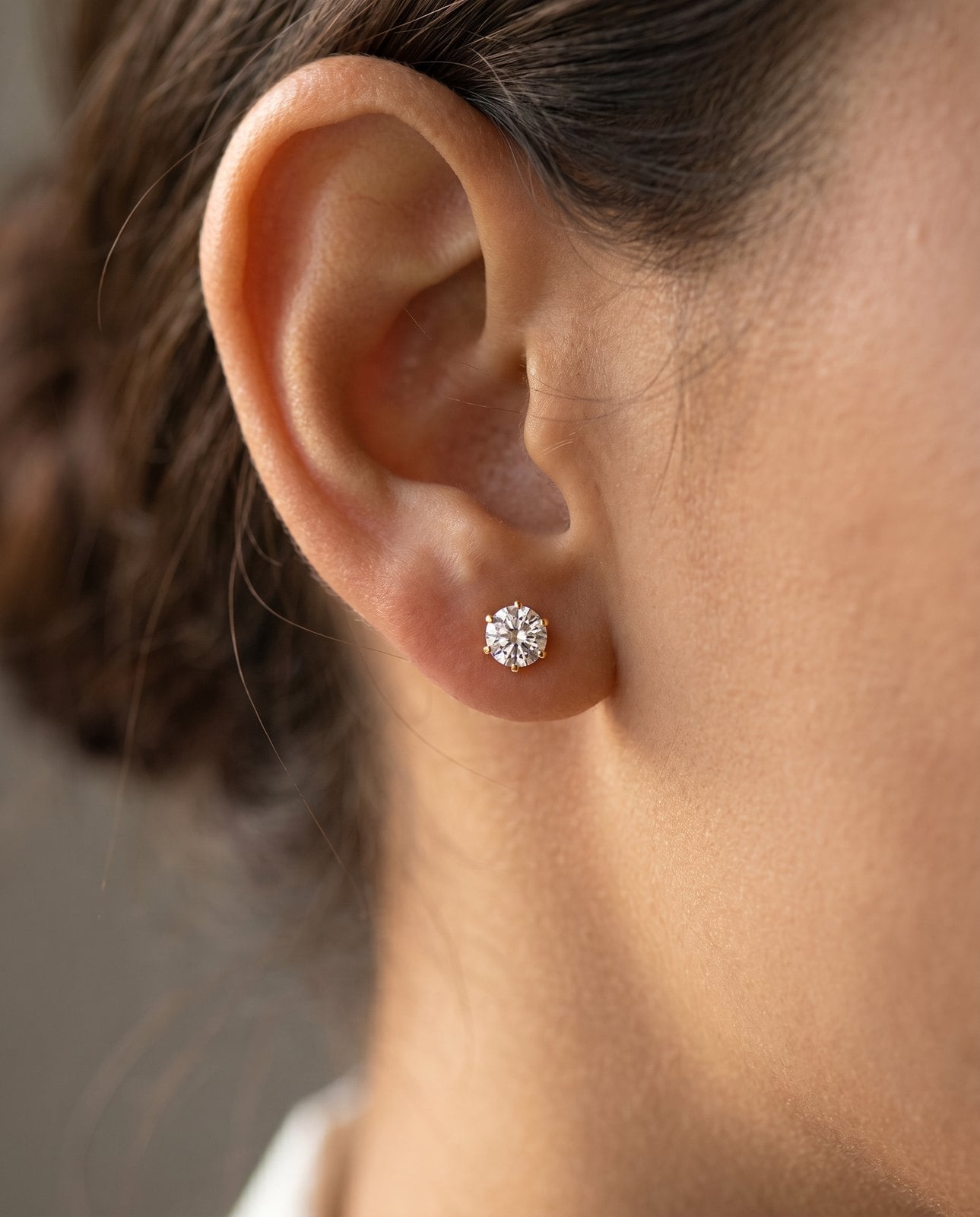 Close crop of an ear wearing small 18K gold-plated stud earrings in soft warm window light