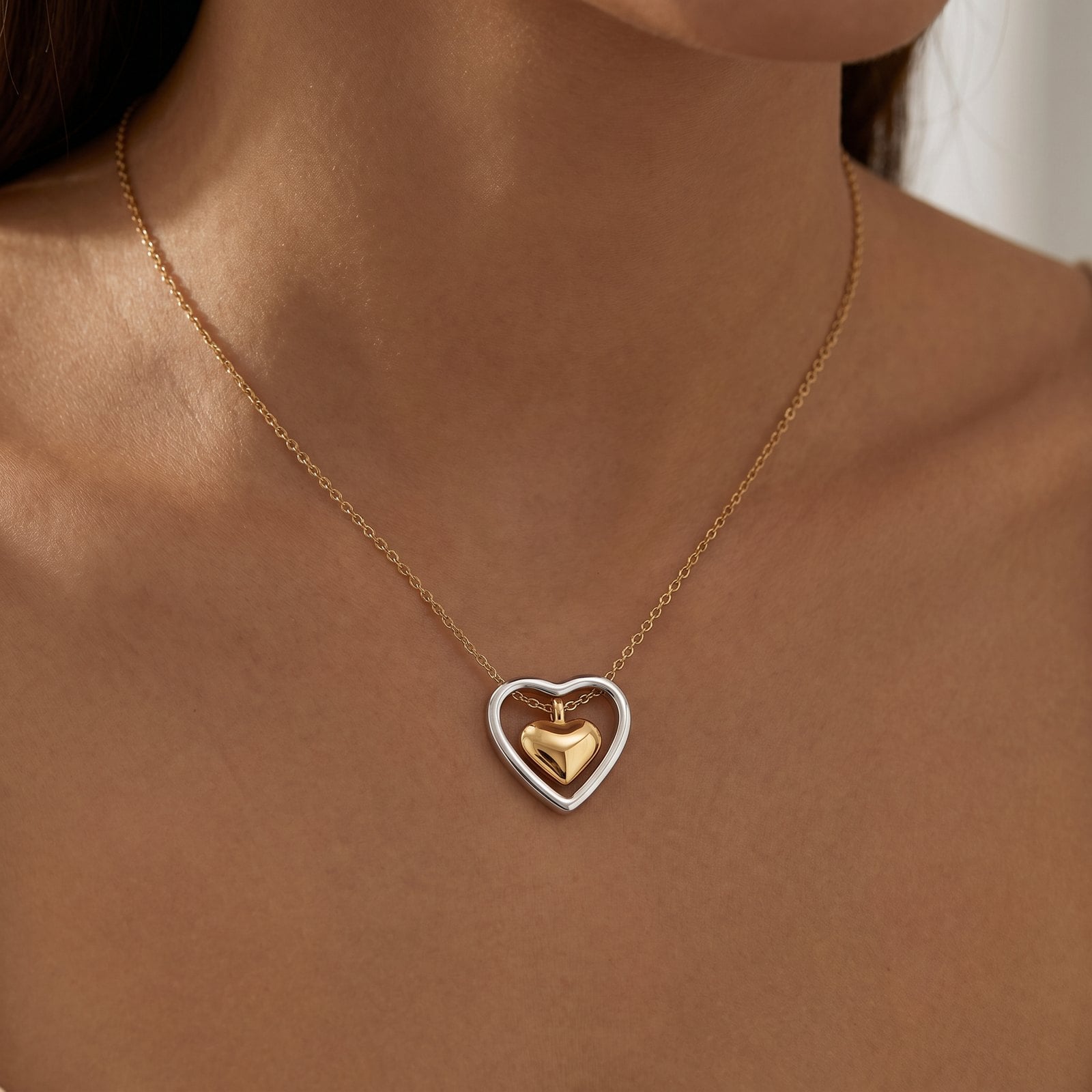 Two-tone gold and silver heart pendant necklace worn at collarbone height on a fine gold chain
