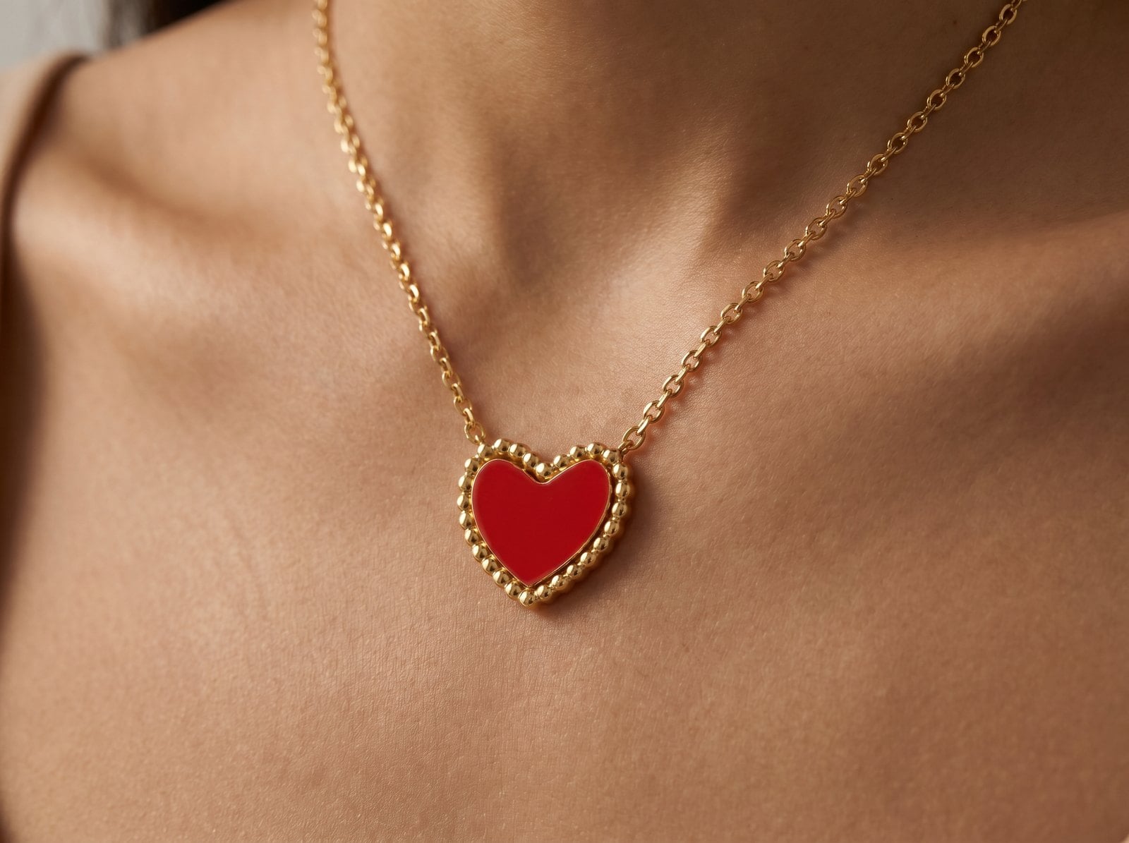 Red heart pendant necklace with a gold bezel on a gold bead-detail chain, worn on the neckline