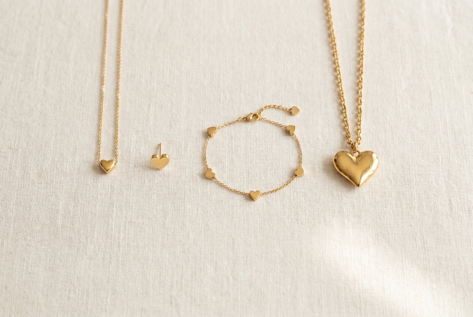 Gold heart jewelry arranged from dainty to statement — a tiny heart pendant, a heart stud, a charm bracelet, and a bold statement heart pendant
