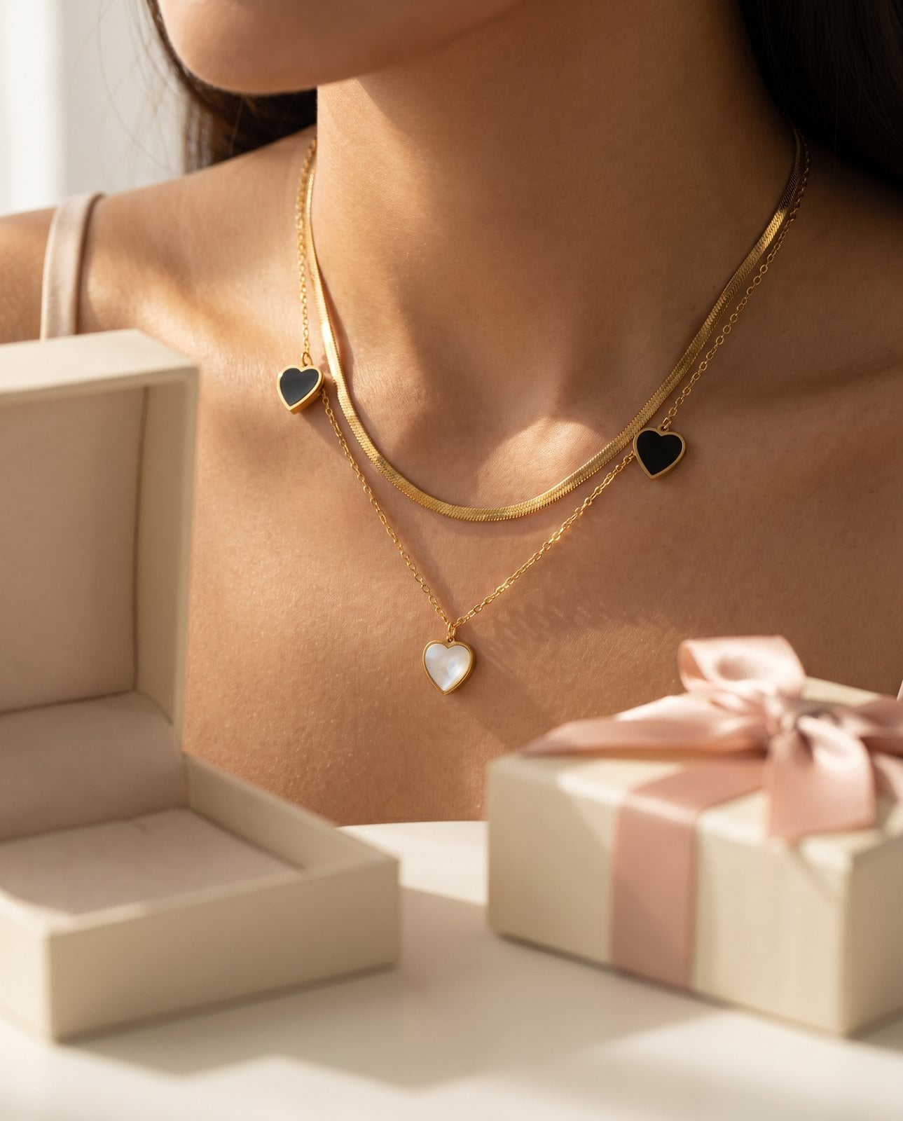 Collarbone view of a woman wearing a dainty gold-plated pendant, open gift box blurred beside her