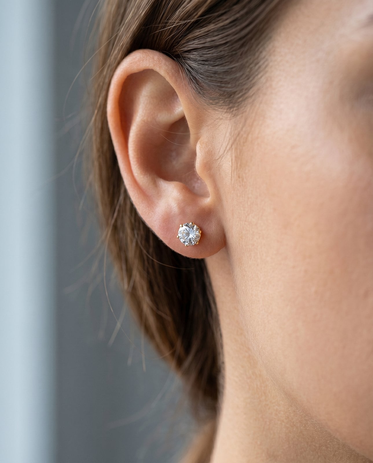 Close-up of a warm-toned ear wearing a dainty gold-plated stainless steel huggie earring in soft light