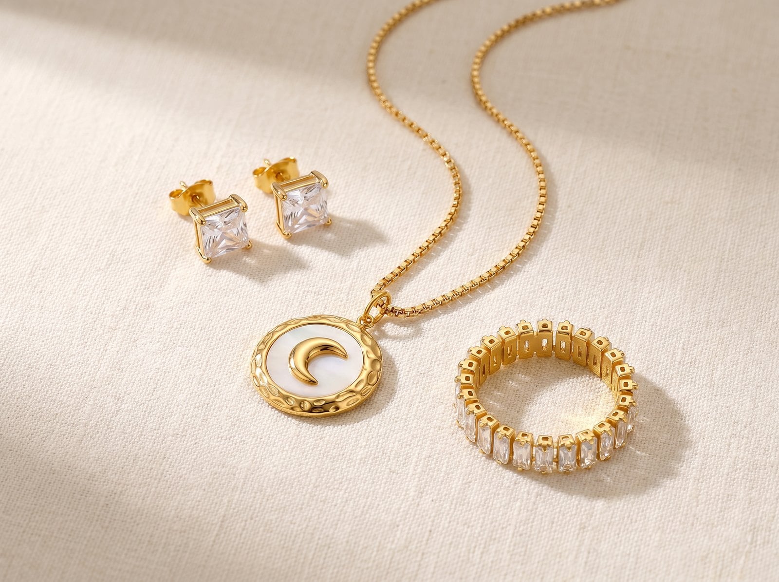 Flat-lay of a small curated set of dainty gold-plated stainless steel jewelry on cream linen