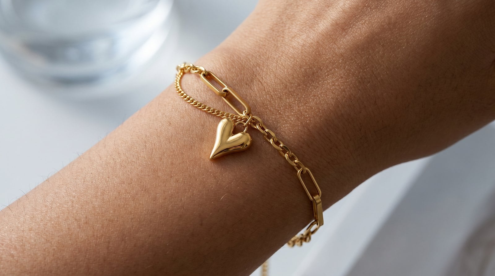 Dainty gold-plated stainless steel chain bracelet resting on a warm-toned inner wrist in soft cool light