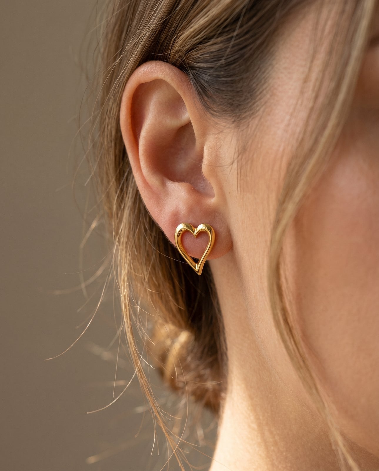 Soft profile close-up of a model's calm unirritated earlobe wearing a dainty gold-plated stud