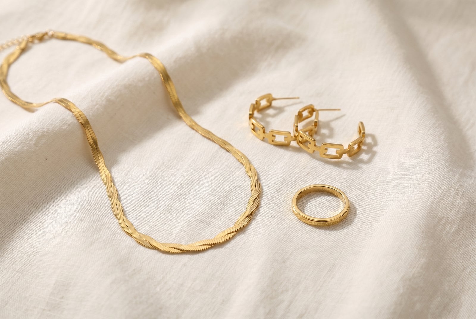 Top-down flat-lay of dainty gold-plated studs, thin necklace and slim ring arranged on cream linen