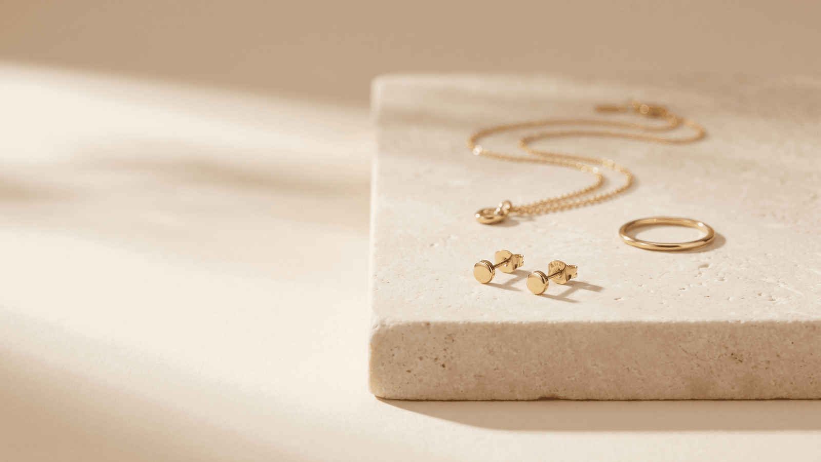 18K gold plated stainless steel earrings and a chain on a cream surface, illustrating nickel-safe jewelry for sensitive skin