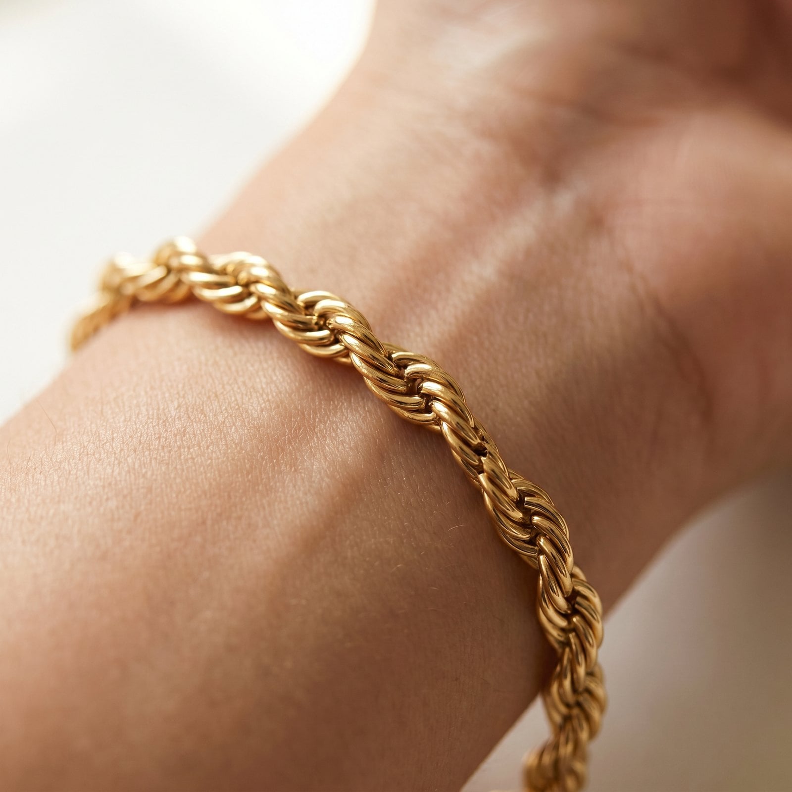 Macro of a fine gold-plated chain link resting on the soft calm skin of a model's inner wrist