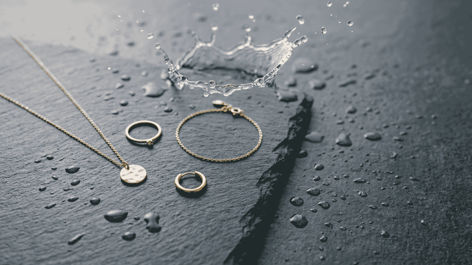 18K gold plated stainless steel jewelry photographed beside water droplets on a stone surface, illustrating waterproof Canadian everyday wear