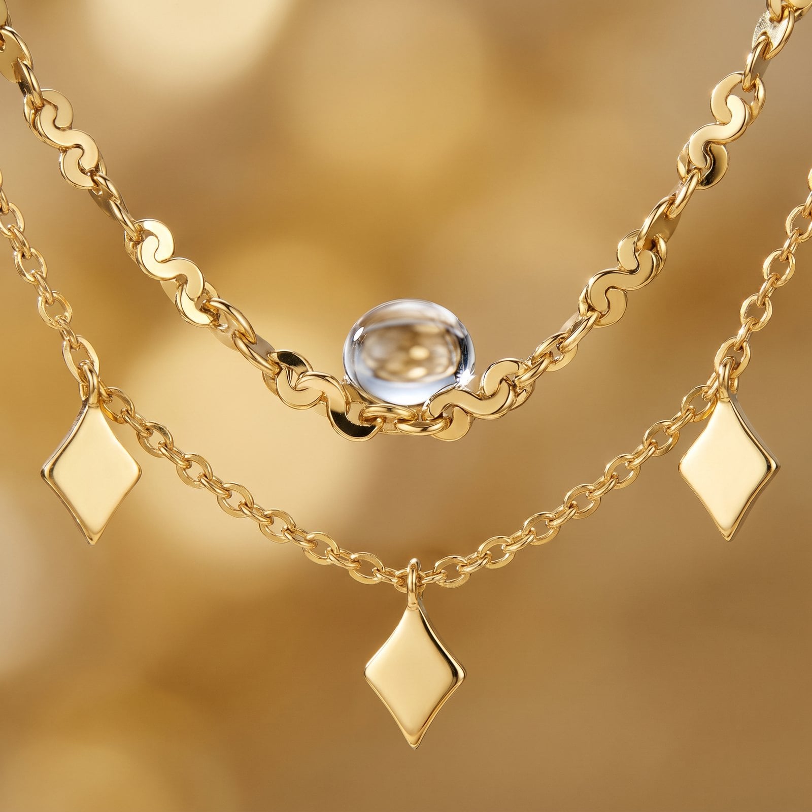 Extreme macro of one crisp water droplet beading on a polished dainty gold-plated chain link.