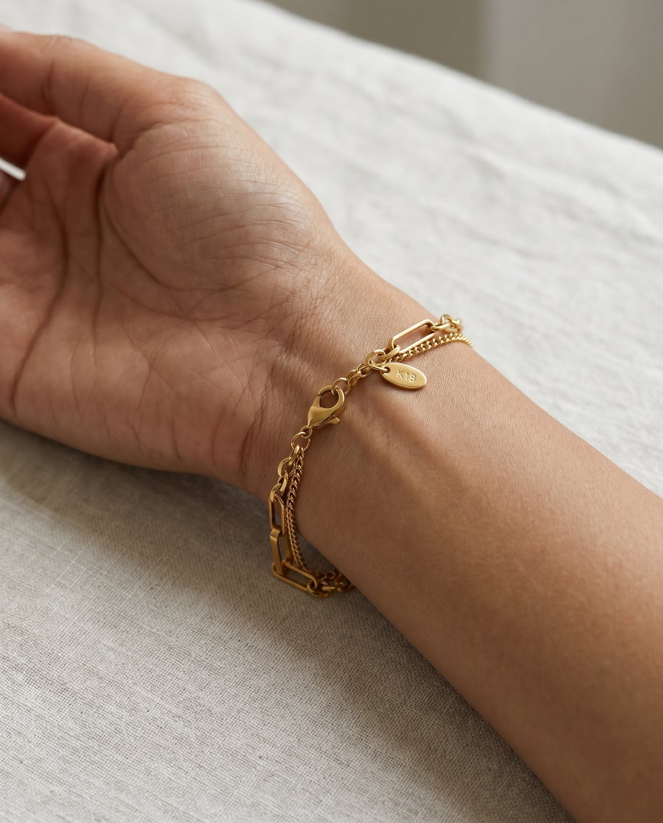 Delicate gold-plated chain bracelet with visible clasp on a warm-neutral-skinned wrist in soft daylight