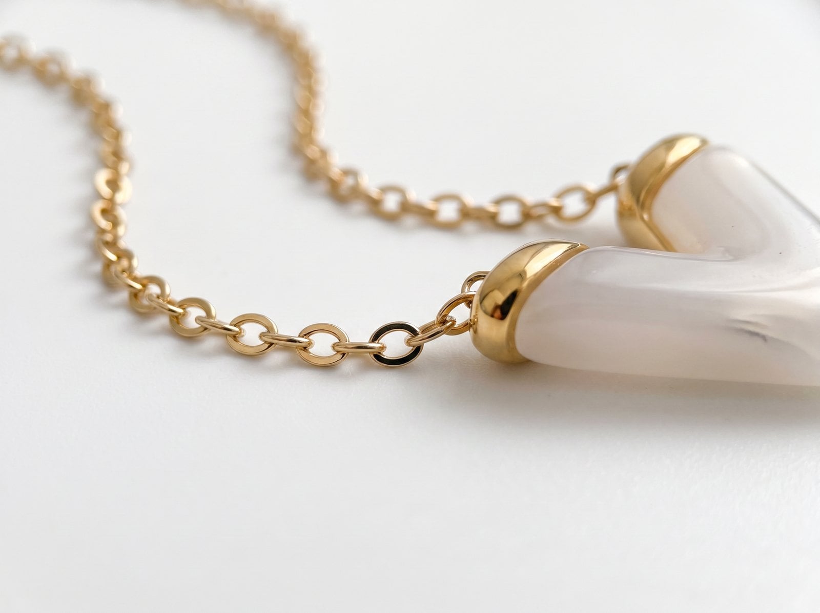 Extreme macro of a fine gold-plated chain link showing the smooth reflective plated surface on white