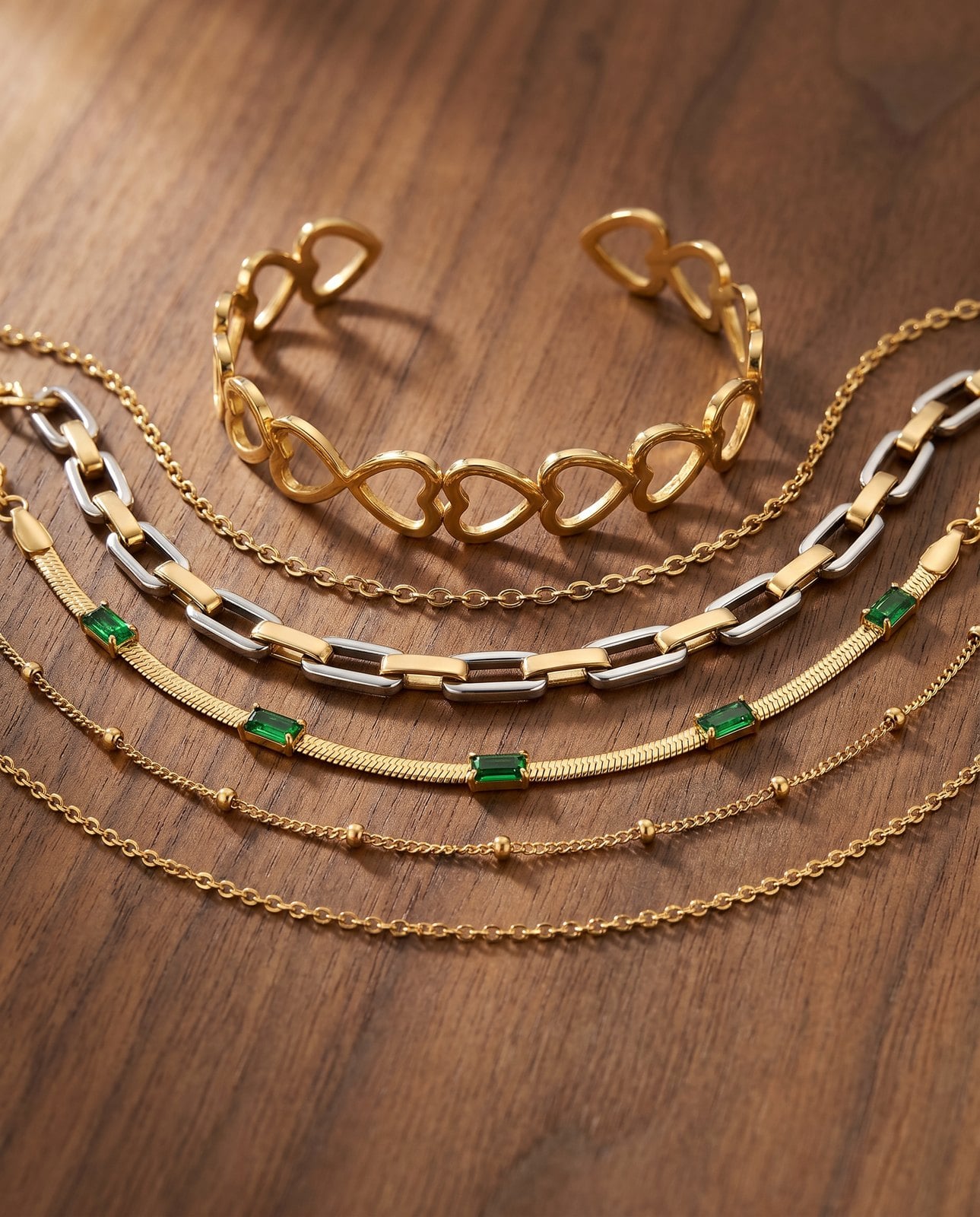 Flat-lay of four gold-plated bracelets with one silver-tone accent and a two-tone bridge piece on walnut wood