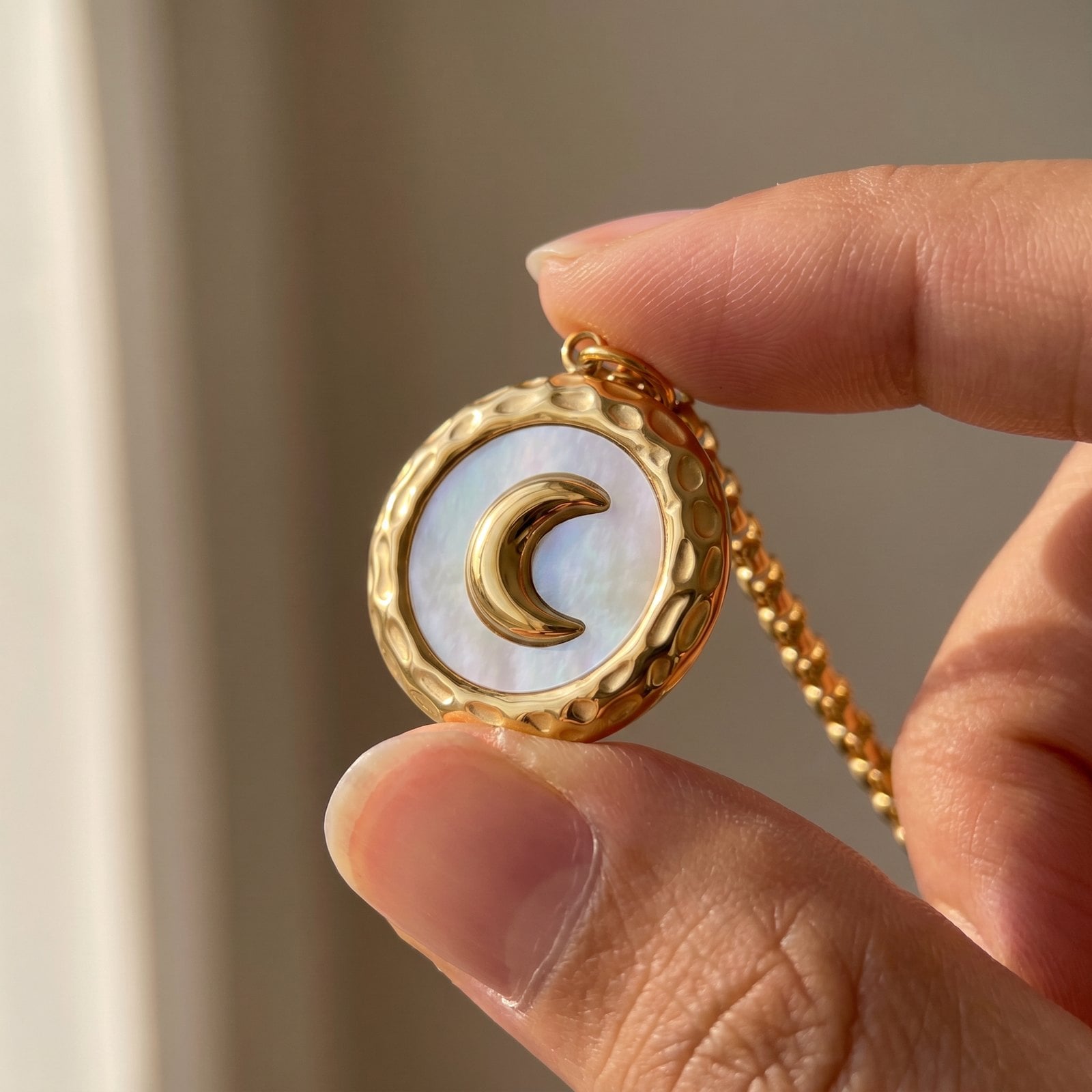 Fingertips turning a tiny gold-plated pendant toward the light to inspect its finish