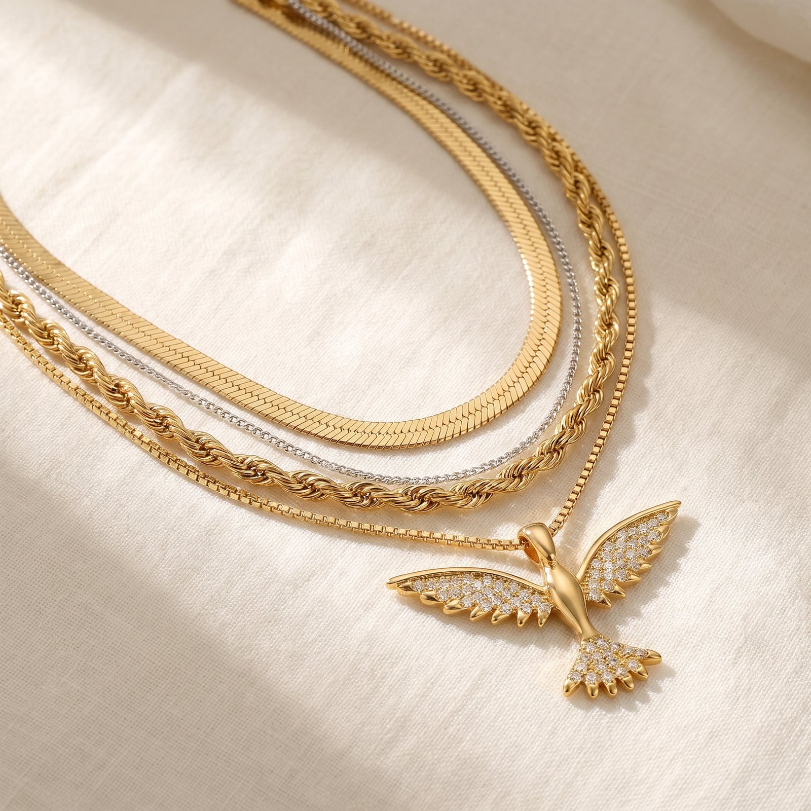 Flat-lay of a layered gold necklace set on cream linen mixing herringbone, rope and box chain textures