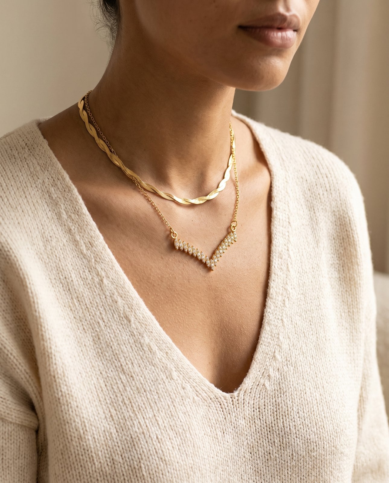 Model in an open V-neck with a layered gold necklace stack cascading into the neckline