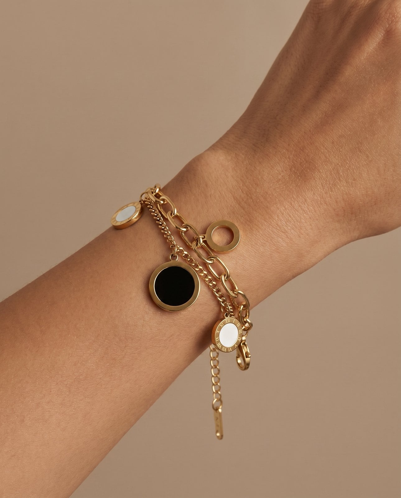 Woman's wrist wearing a gold-plated charm bracelet with tiny butterfly, heart and clover symbol charms