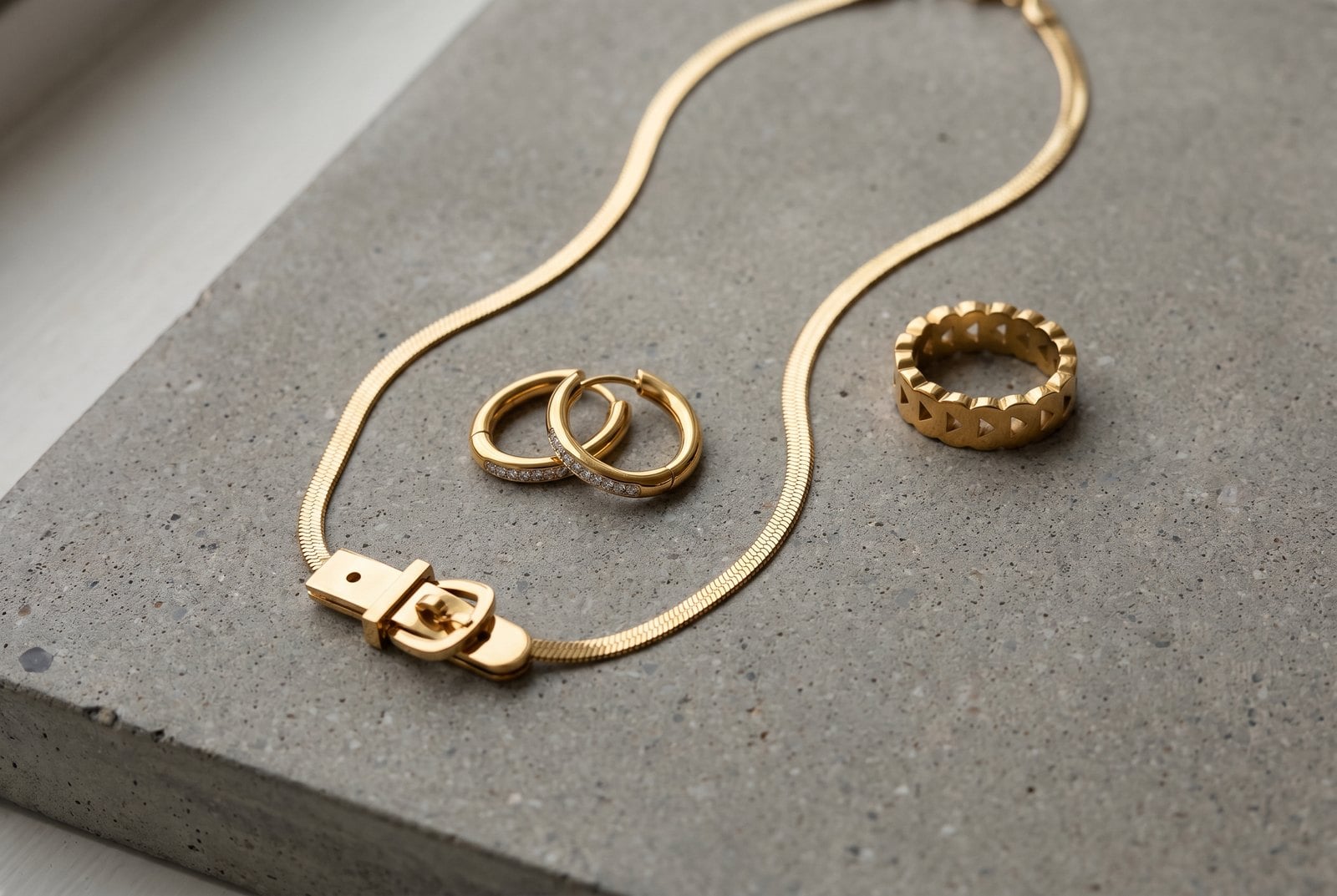 Medium-weight gold-plated curb chain, hoops and signet ring flat-lay on grey concrete