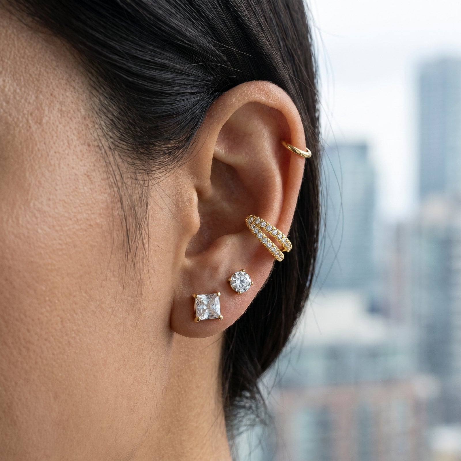 Curated ear stack of small gold studs, a small hoop and an ear cuff on a tucked-back ear