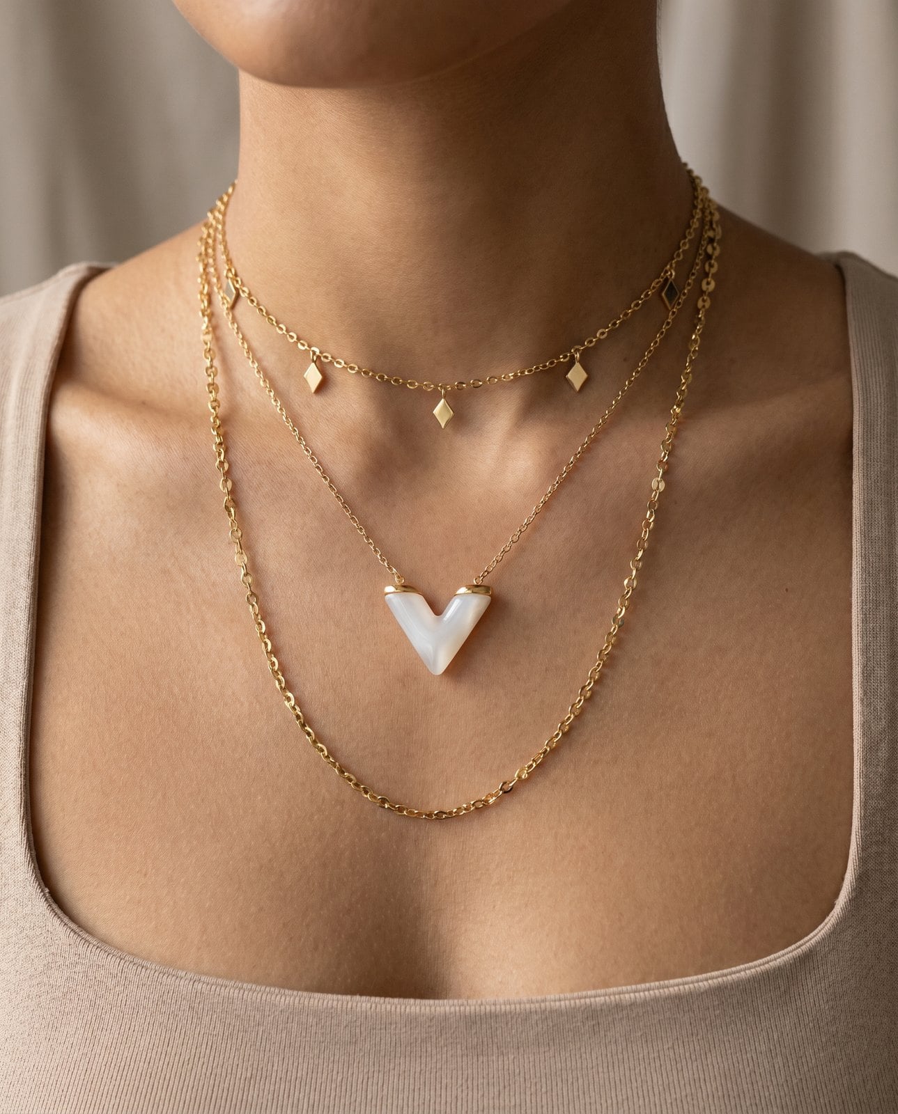 Collarbone wearing a three-piece layered gold necklace stack at choker, princess and matinee lengths