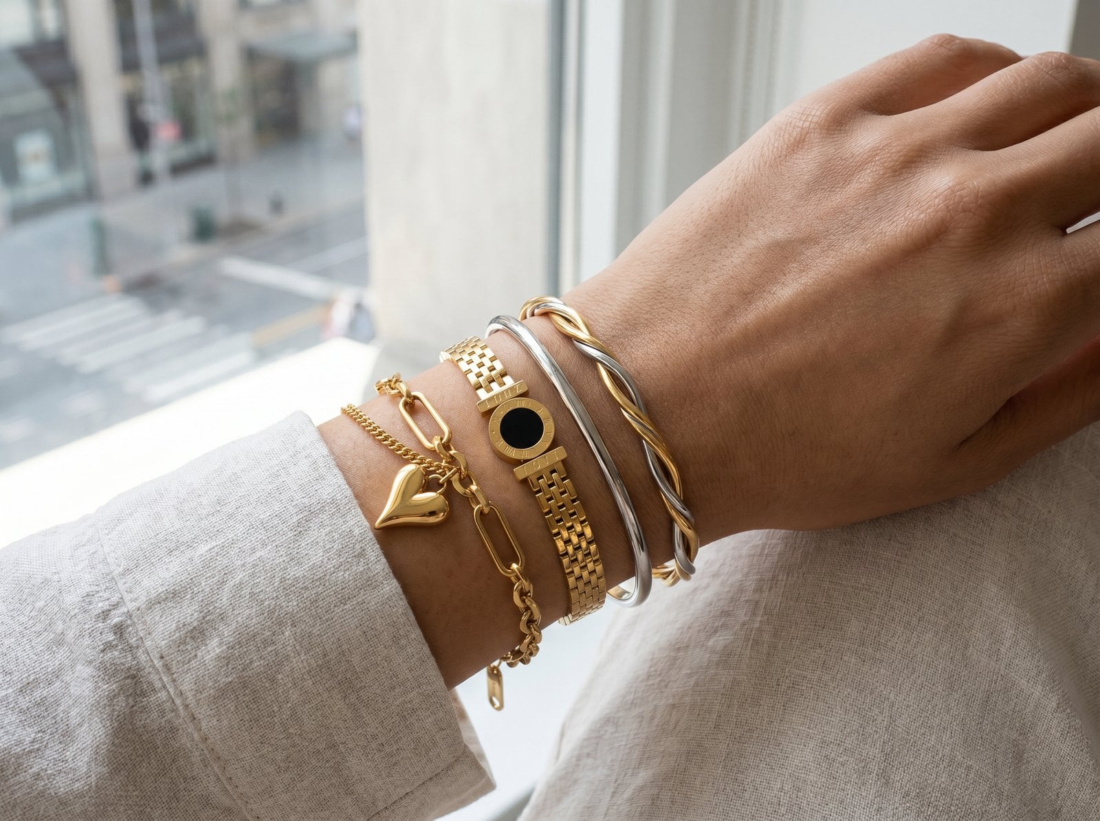 Wrist wearing a gold-dominant stack with one silver bangle and a two-tone bridge bracelet