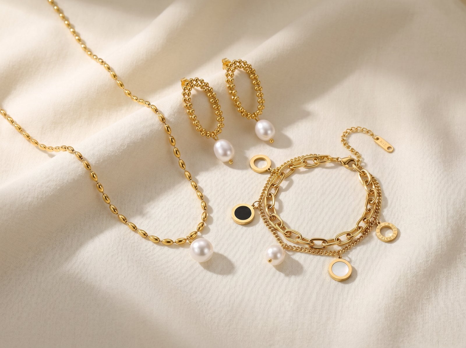 Flat-lay of gold-plated chain, hoop and bracelet each with a single pearl accent on cream linen