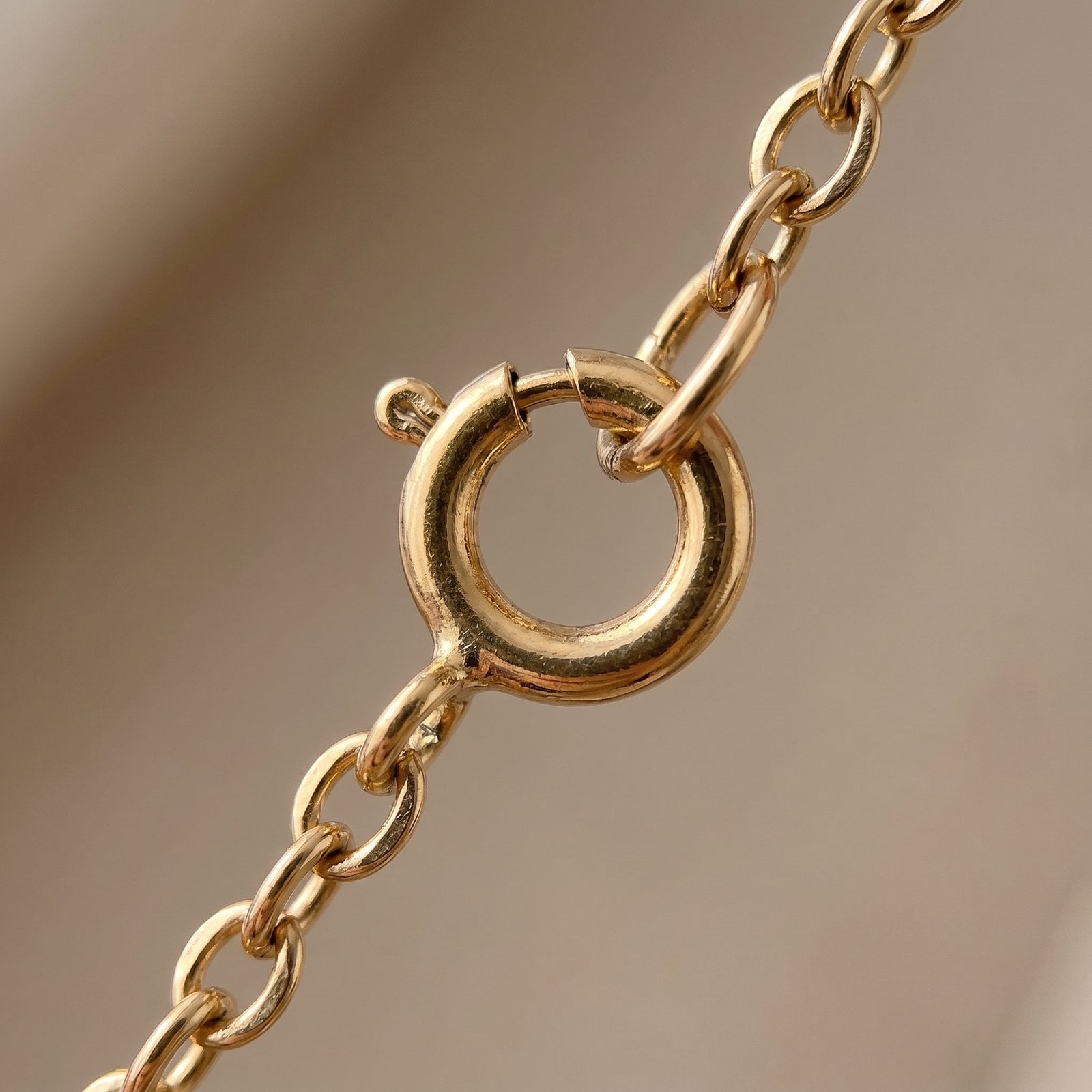 Close-up macro of the spring-ring clasp and links of a delicate 18K gold-plated chain, plating intact