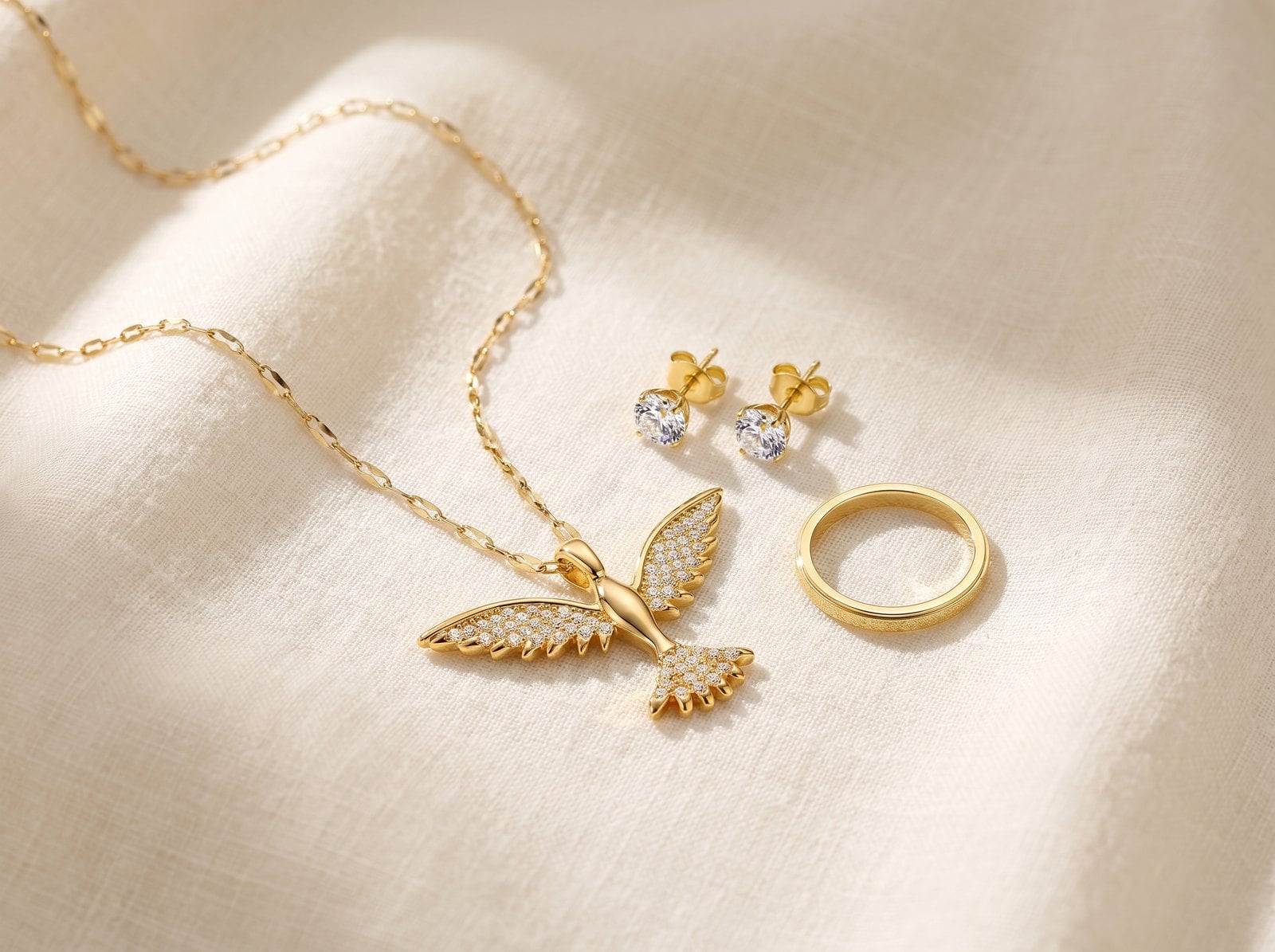 Overhead flat-lay of an 18K gold-plated necklace, bracelet and stud earrings set on cream linen