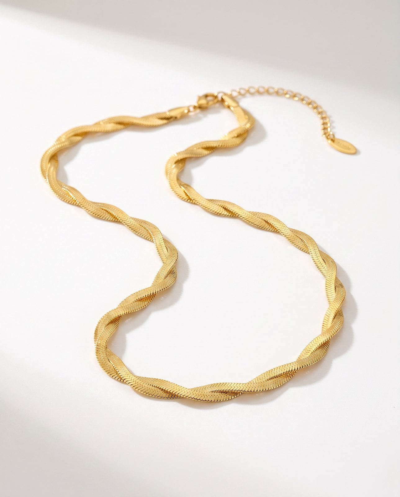 Single dainty 18K gold-plated cable chain necklace laid in an S-curve on a clean white studio surface